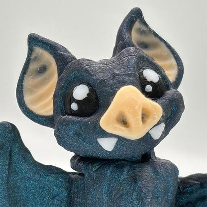 Close-up of a 3D-printed toy vampire bat figure with a sparkling blue-black filament.